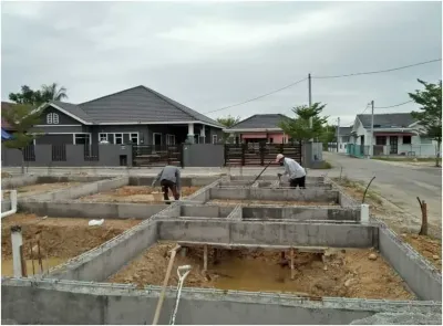 Kerja tapak rumah RumahHQ di peringkat asas — pekerja meratakan tanah di antara rasuk tanah konkrit yang sudah siap, di kawasan perumahan berjalan raya