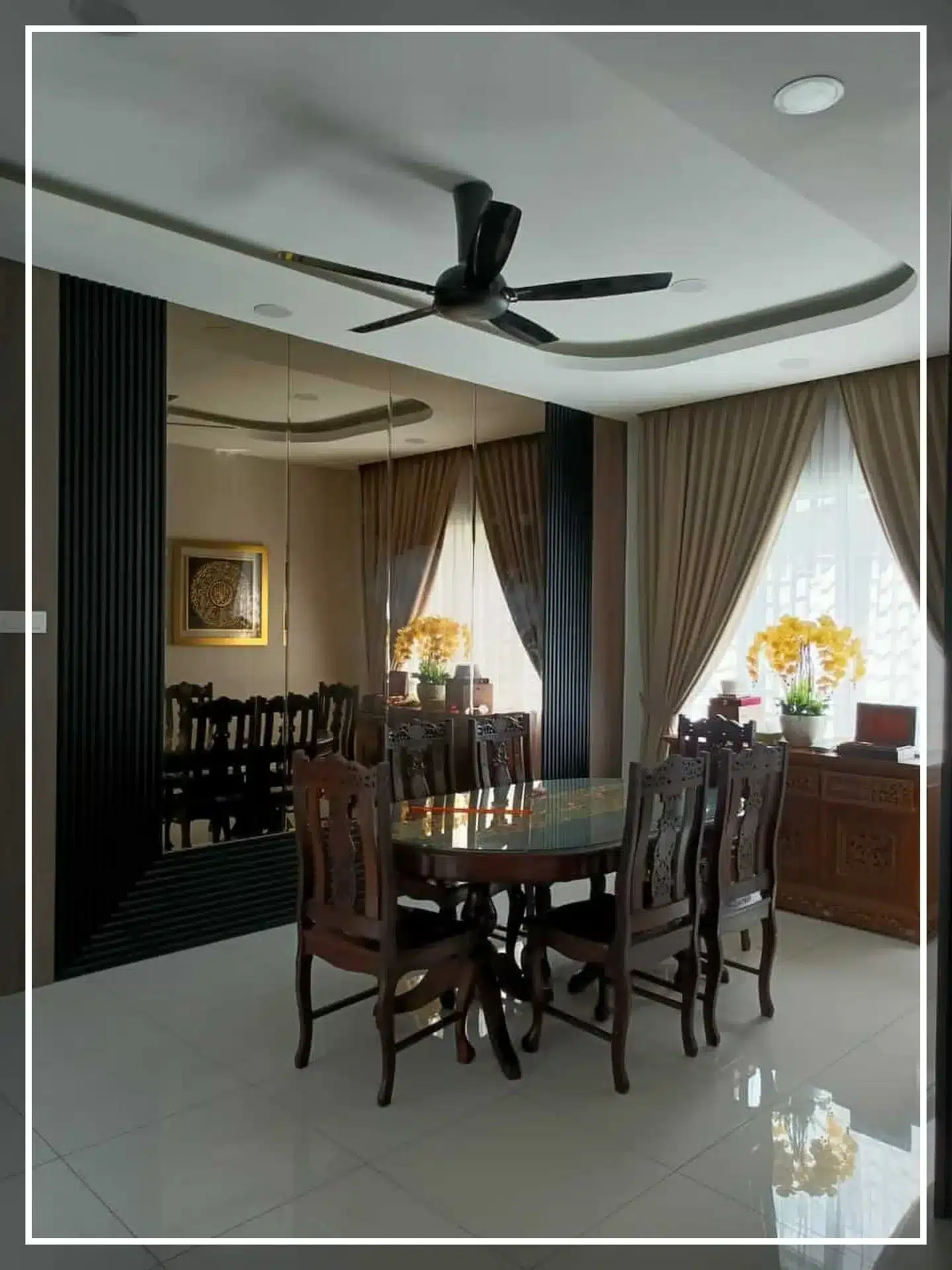 Elegant dining room with round wooden table, ornate chairs, mirrored wall, and ceiling fan, accented by floral decor.