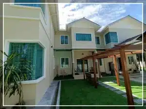 Modern two-story house with garden pergola and lush green lawn under a blue sky.