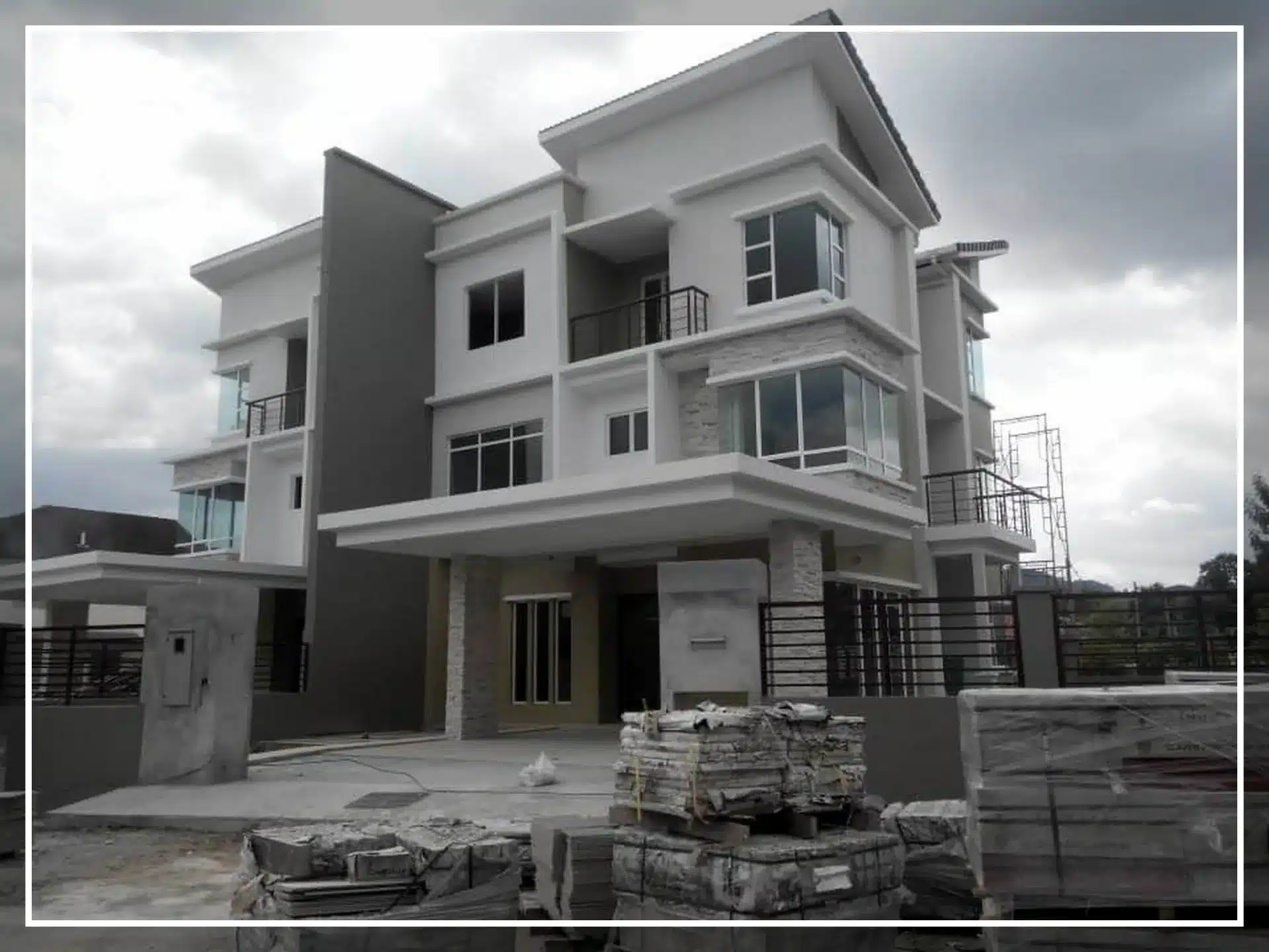 Modern two-story house under construction with glass windows and grey accents, featuring an unfinished driveway.