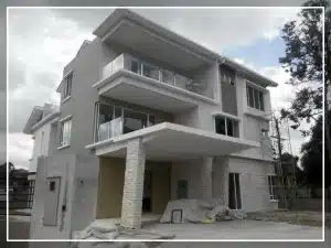Modern three-story house with large glass windows and spacious balconies under a cloudy sky.