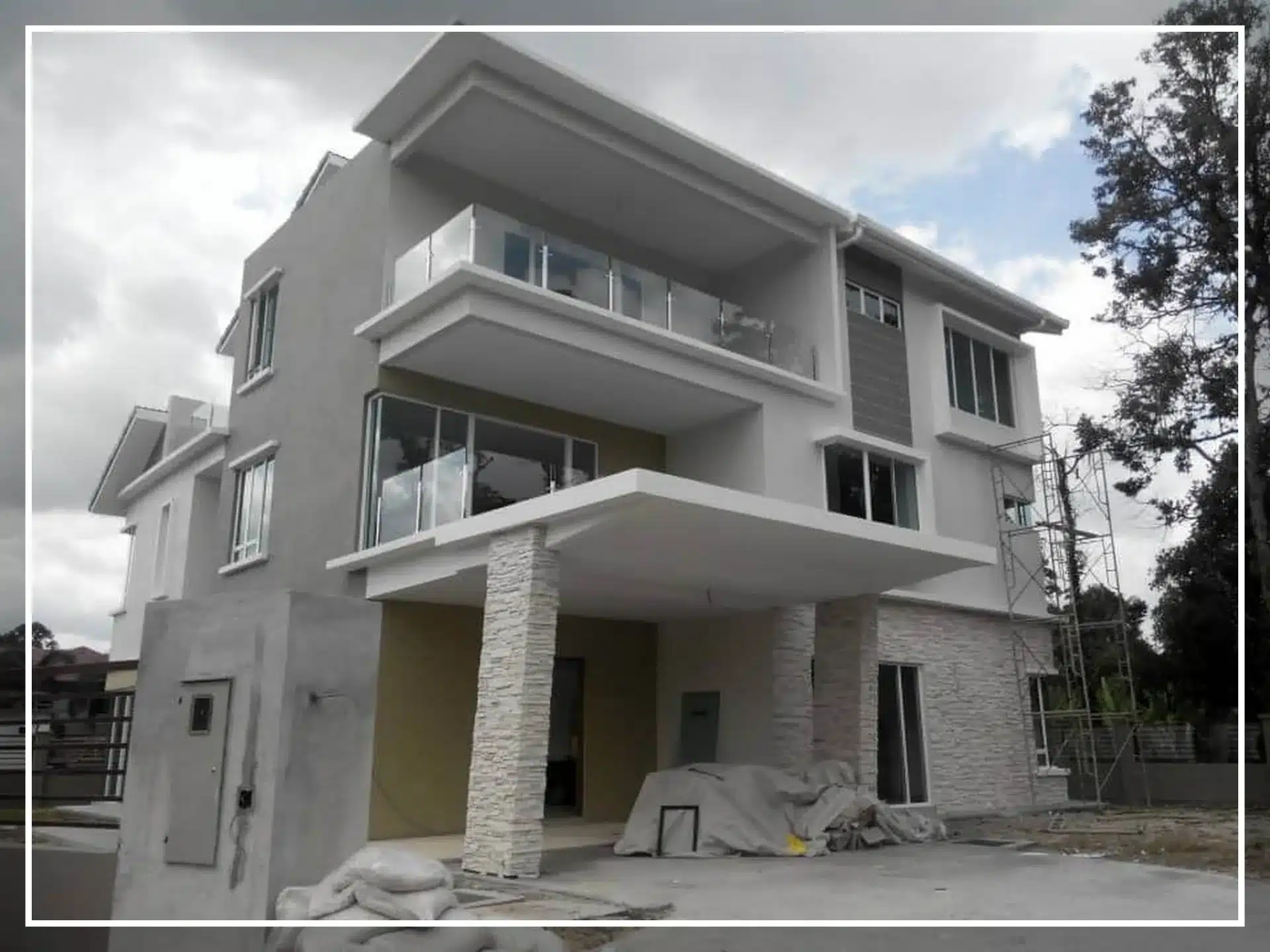 Modern three-story house with large glass windows and spacious balconies under a cloudy sky.