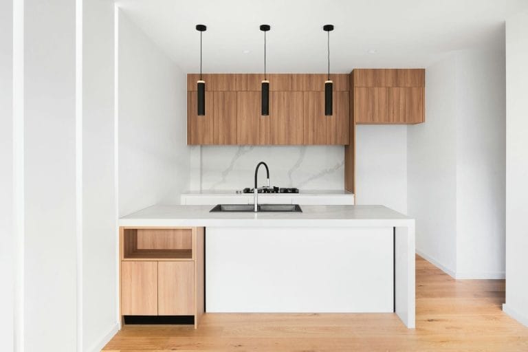Modern kitchen with wooden cabinets, white countertops, and sleek black pendant lights above an island sink.