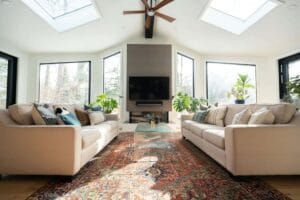 Modern living room with skylights, cozy couches, vibrant rug, and indoor plants for a bright, inviting space.