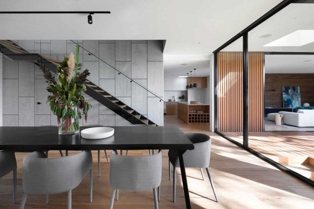 PANDUAN KOMPREHENSIF BINA RUMAH ATAS TANAH SENDIRI DI MALAYSIA 4 Modern open-plan dining room with elegant decor, wooden elements, and staircase for a stylish home interior.