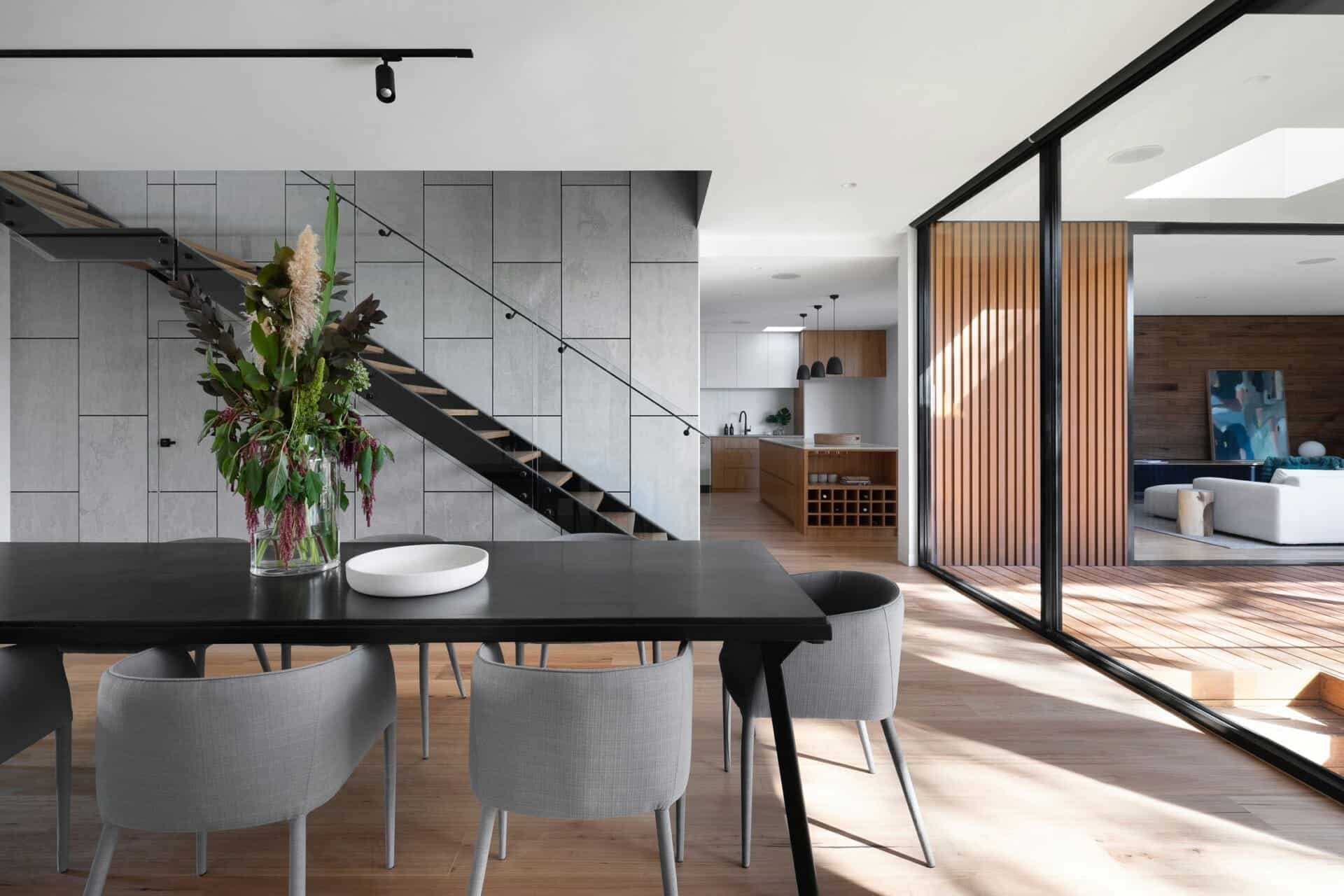Modern open-plan dining area with stylish decor, natural light, and sleek staircase design.