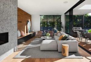 Modern living room with cozy sofa, wooden accents, floor-to-ceiling windows, and patio access for indoor-outdoor living.