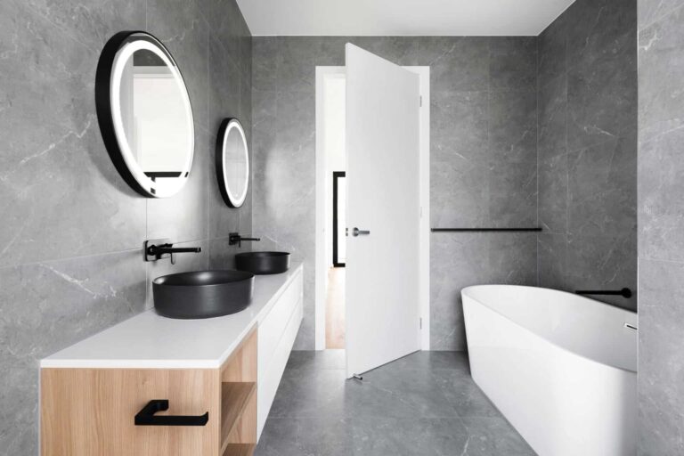 Transformasi Impian: Kontraktor Ubahsuai Rumah Terbaik di Bangi 1 Modern bathroom with grey tiled walls, round mirrors, black vessel sinks, and a sleek white freestanding bathtub.