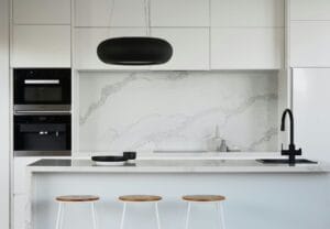 Modern kitchen with white marble countertops, minimalist design, black pendant light, and wooden bar stools.